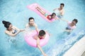 Family and friends playing in the water at the pool with inflatable tubes Royalty Free Stock Photo