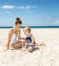 Smiling mother and girl in swimsuits at sandy beach playing Royalty Free Stock Photo