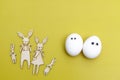 Family of funny hares cut out of plywood are on the yellow background. A cheerful white eggs with eyes . Creative image. Easter