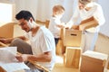Father assembling furniture in living room of new apartment, mother with son and pile of moving boxes on background Royalty Free Stock Photo