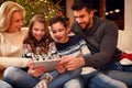 Family gathered around a Christmas tree and using tablet