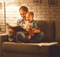 Family before going to bed mother reads to her baby son book near a lamp in the evening. Royalty Free Stock Photo