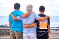 Family group, three males, father, adult son and teen grandson embracing each other looking at horizon over water