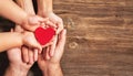 Family hands holding red heart on wooden background. Donation, charity, health concept.