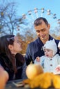 family has picnic in autumn city park, father and daughters, children and parent sitting together at the table, with apples and