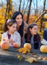 family has picnic in autumn city park, moher and daughters, children and parent sitting together at the table, with apples and