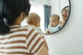 Asian mother playing and laughing her little newborn baby son while looking at their faces in mirror at home Royalty Free Stock Photo