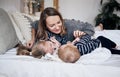 Family having fun at home. Happy young mother playing with children in bedroom. Brother and sister embracing on the bed. Sunny hol Royalty Free Stock Photo