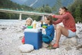 Family having a picnic in nature out of a cool box, sitting on the river bank