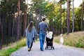 Family holding hands walking together along forrest path with their daughter, father pushing the pram