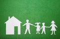 Family and home concept. Parents and children holding hands. Paper family figures and house on green textural background