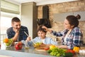 Family at home leaning on table in kitchen together parents looking at son mixing salad smiling proud Royalty Free Stock Photo