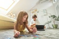 Family at home. Little girl lying on the floor in the living room and playing with puzzles while her brother using Royalty Free Stock Photo