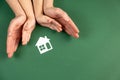 Family home and real estate concept. Close up of female and child hands holding white paper house and heart on green background. Royalty Free Stock Photo