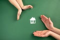 Family home and real estate concept. Close up of female and child hands holding white paper house and heart on green background. Royalty Free Stock Photo