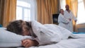 A family in the hotel room - a little girl sleeping in bed - her mom and dad looking at her and opening the curtains Royalty Free Stock Photo