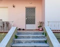 A family house entrance stairs to a small terrace, white door and pale pink wall.