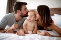 Family with kid in the morning. Mother, father kissing baby child on a white bed. Royalty Free Stock Photo