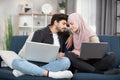 Family, love, gadgets and relaxation at home concept. Happy young muslim couple, sitting on blue sofa at home touching