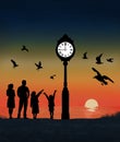 A family, mom, dad and kids are seen with a flock of seagulls on the beach where a lighted clock is seen at sunSet