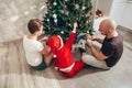 Family - mom, dad and son in a Santa costume are sitting under the Christmas tree on the floor in their apartment and decorating Royalty Free Stock Photo