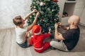 Family - mom, dad and son in a Santa costume are sitting under the Christmas tree on the floor in their apartment and decorating Royalty Free Stock Photo