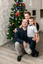 Family - mom, dad and son in smart clothes are sitting next to the Christmas tree in their new apartment, looking at the camera Royalty Free Stock Photo