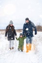 Family mom, dad and toddler walk on a snowy road. Parents walk with their child holding a hand in winter Royalty Free Stock Photo