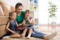 Happy mother and little daughters reading a book together in the living room at home. Family activity concept. Royalty Free Stock Photo