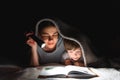 Family Mom and little son reading a book with a flashlight under the blanket Royalty Free Stock Photo