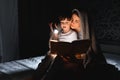 Family Mom and little son reading a book with a flashlight under the blanket Royalty Free Stock Photo