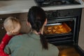 Family, Mom with toddler baby girl cooking gingerbread and puts cookies in oven. Christmas homemade gingerbread biscuit Royalty Free Stock Photo