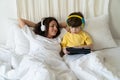 Family morning in bedroom: mom in headphones look at little kid son play games on tablet computer Royalty Free Stock Photo