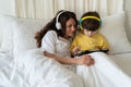 Family morning in bedroom: mom in headphones look at little kid son play games on tablet computer Royalty Free Stock Photo