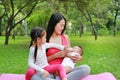 Family of mother and daughter feeding milk for infant from bottle in the green garden