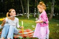 Young mother with her cute little girl is blowing a soap bubbles in summer park. Royalty Free Stock Photo