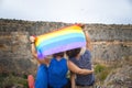 Family mother, daughter and son, with a dog on top of a cliff sitting backwards unrecognizable, waving a rainbow flag in the wind Royalty Free Stock Photo