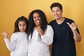 Family of mother, daughter and son standing over yellow background pointing to the back behind with hand and thumbs up, smiling Royalty Free Stock Photo