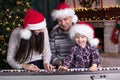 Family - mother, father and kid wearing santa hats playing the piano over christmas background Royalty Free Stock Photo