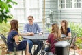 A family of a mother and father and two daughters sitting outside at a patio table with an umbrella Royalty Free Stock Photo