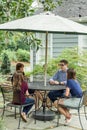 A family of a mother and father and two daughters sitting outside at a patio table with an umbrella Royalty Free Stock Photo