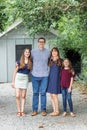 A family of a mother and father and two daughters standing outside in front of a small storage building