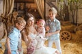 family of a mother with two sons and a baby stands in front of the wooden doors leading to a barn, feeding a white baby goat