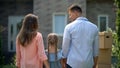 Family moving in, looking at each other in front of new house, back view