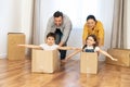 Family moving in new home. Multiracial family of four have fun in new house, parents riding kids in cardboard boxes in Royalty Free Stock Photo