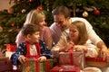 Family Opening Christmas Present In Front Of Tree