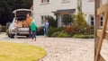 Family Outside New Home On Moving Day Unloading Boxes From Car As Son With Skateboard Runs To Help Royalty Free Stock Photo