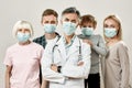 Family Physician. Portrait of mature male doctor and family of four wearing medical protective masks, looking at camera