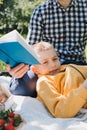 Family picnic. Dad and son in a green garden in sunny weather on a picnic eating pizza and reading book Royalty Free Stock Photo