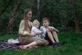 Family picnic at garden park outdoors. Mother, eldest son and youngest child sitting on picnic blanket